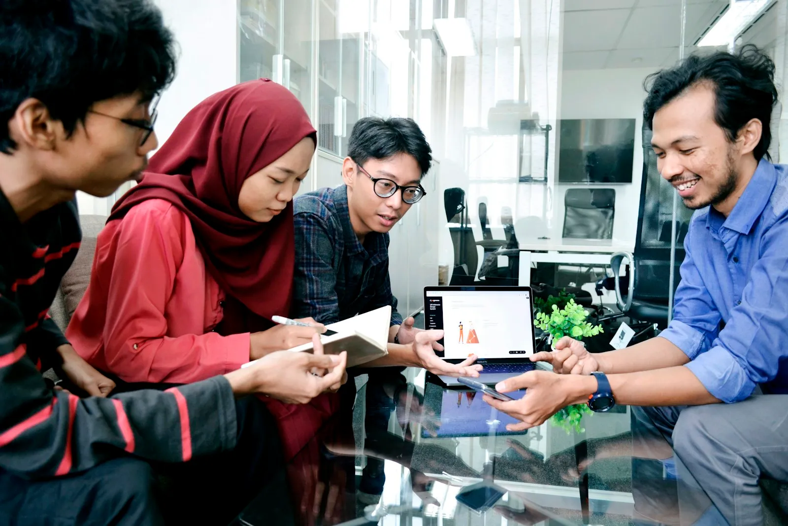 Empat orang berkolaborasi di sekitar laptop dan printer